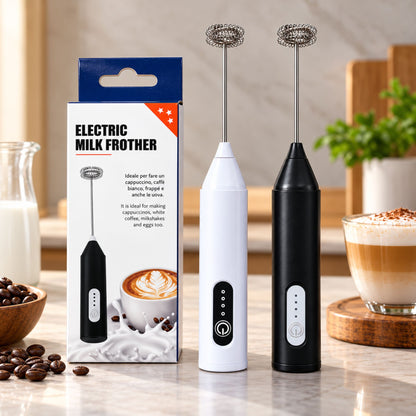 Two electric milk frothers standing on a countertop beside their retail box, with coffee cups and coffee beans in a kitchen setting. The frothers are shown in white and black, with the box labeled 'ELECTRIC MILK FROTHER'.