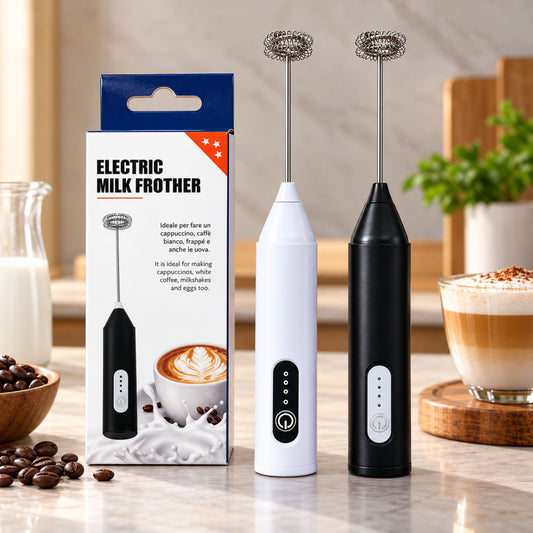 Two electric milk frothers standing on a countertop beside their retail box, with coffee cups and coffee beans in a kitchen setting. The frothers are shown in white and black, with the box labeled 'ELECTRIC MILK FROTHER'.
