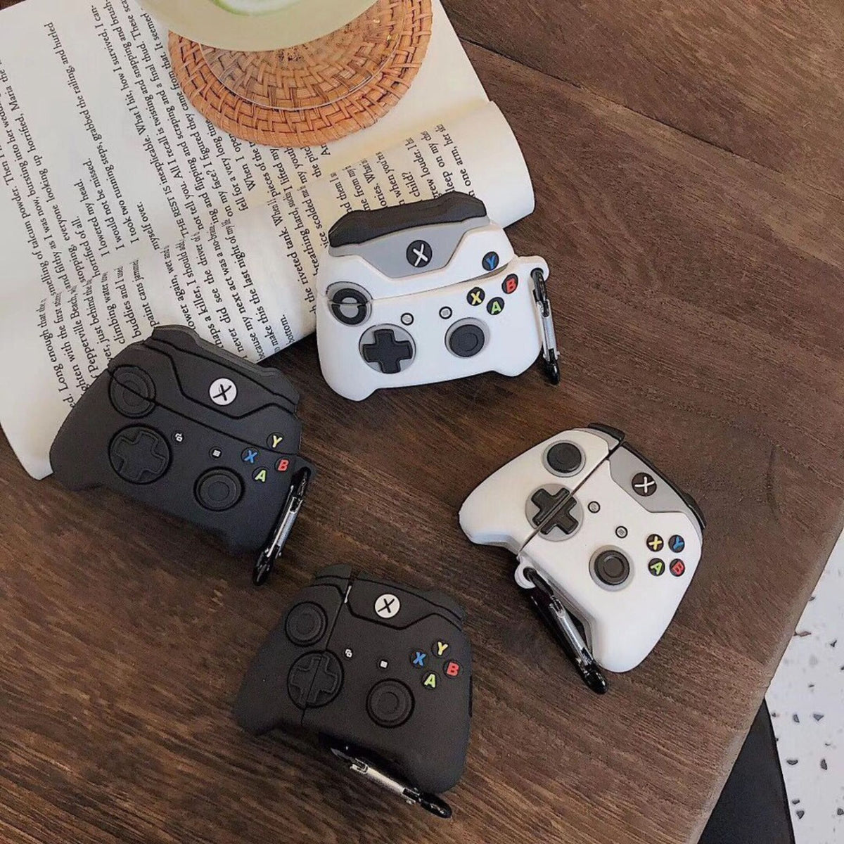 Four gaming controllers in black and white on a wooden surface with books underneath.